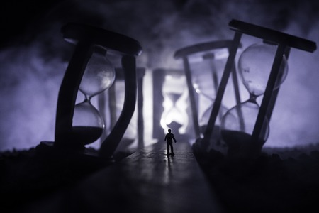 Time concept. Silhouette of a man standing between hourglasses with smoke and lights on a dark background. Surreal decorated pictureの写真素材