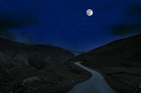 Mountain Road through the forest on a full moon night. Scenic night landscape of country road at night with large moonの写真素材