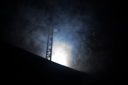 Abstract Industrial background with construction crane silhouette over amazing night sky with fog and backlight. Tower crane against the foggy sky at night. Industrial skyline. Selective focusの写真素材