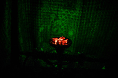 Hookah hot coals on shisha bowl on dark foggy background. Stylish oriental shisha. Creative concept