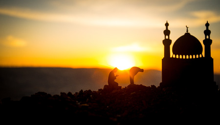 Concept of religion Islam. Silhouette of man praying on the background of a mosque at sunset. Festive greeting card, invintation for Muslim Holidayの写真素材