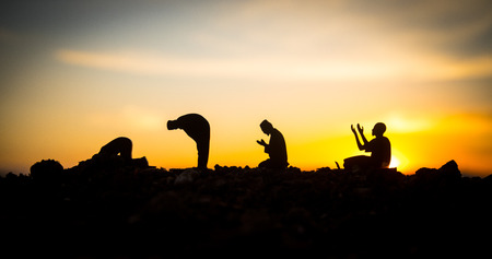 Concept of religion Islam. Silhouette of man praying on the background of a mosque at sunset. Festive greeting card, invintation for Muslim Holidayの写真素材