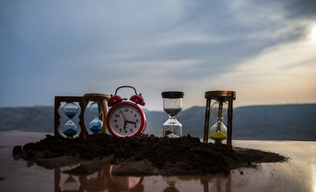 Hourglasses and red alarm clock during sunset. Time concept. Selective focus.