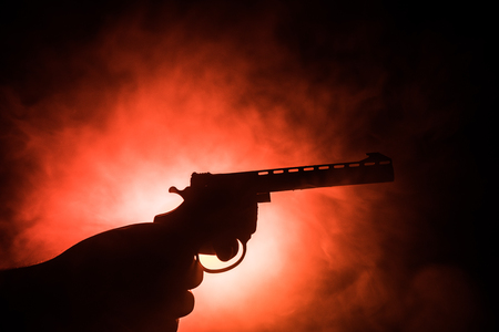 Male hand holding gun on black background with smoke toned back lights. Silhouette of a gun in hand. Crime concept. Selective focusの写真素材