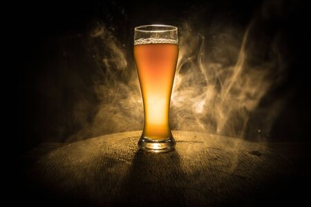 Creative concept. Single beer glass on wooden table at dark toned foggy background. Selective focusの写真素材