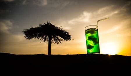 Close up wet glass of green cold mint drink, colorful orange sunset background on the terrace. Cooling summer drink. Summer fresh and cooling inspiration, evening contrast color combination. Relax.の写真素材