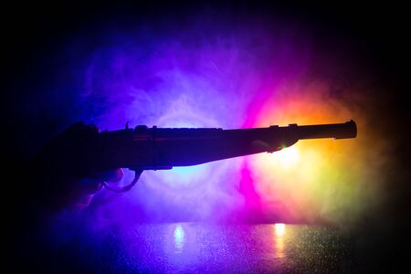 Male hand holding vintage gun on black background with smoke toned back lights. Silhouette of a gun in hand. Crime concept. Selective focusの写真素材