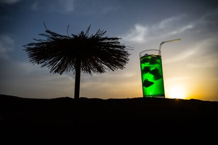 Close up wet glass of green cold mint drink, colorful orange sunset background on the terrace. Cooling summer drink. Summer fresh and cooling inspiration, evening contrast color combination. Relax.の写真素材
