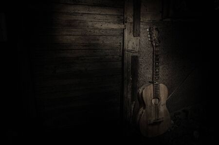 An wooden acoustic guitar is against a grunge textured wall. The room is dark with a spotlight for...