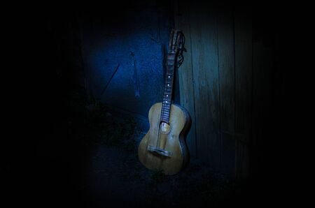 An wooden acoustic guitar is against a grunge textured wall. The room is dark with a spotlight for your copyspace. old broken guitarの写真素材