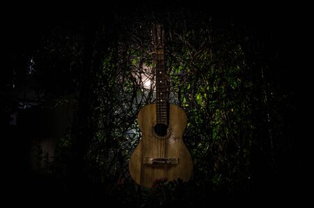 An wooden acoustic guitar at night. with spotlight for your copyspace. old broken guitar