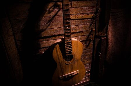 An wooden acoustic guitar is against a grunge textured wall. The room is dark with a spotlight for your copyspace. old broken guitarの写真素材