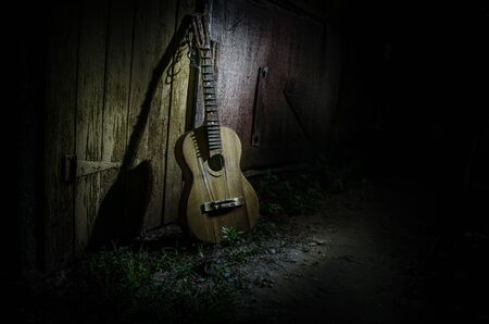 An wooden acoustic guitar is against a grunge textured wall. The room is dark with a spotlight for your copyspace. old broken guitarの写真素材