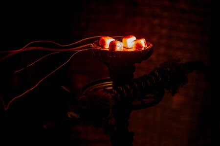 Hookah hot coals on shisha bowl on dark foggy background. Stylish oriental shisha. Creative concept
