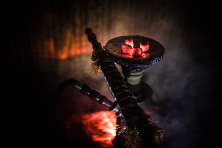 Hookah hot coals on shisha bowl on dark foggy background. Stylish oriental shisha. Creative concept