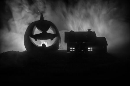 Horror view of Halloween pumpkin with scary smiling face. Head jack lantern with haunted building and tree on dark toned foggy background.の写真素材