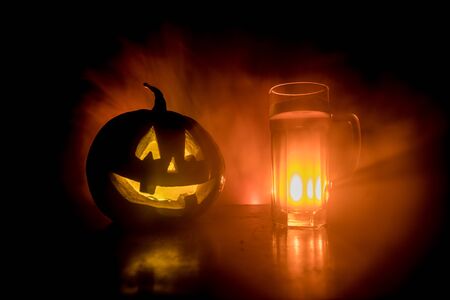 Glass of cold light beer with pumpkin on a wooden table for Halloween. Glass of fresh beer and pumpkin on a dark toned foggy backgroundの写真素材