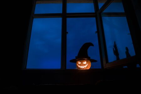 Scary Halloween pumpkin in the mystical house window at night or halloween pumpkin in night on room with blue window. Symbol of halloween in window. Selective focusの写真素材