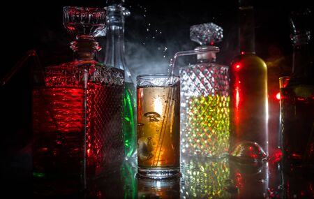 Multicolored glasses filled with alcoholic drinks, with splases of ice cubes falling inside, standing on the mirror surface. Black background. Conceptual, celebrated, commercial design. Closeup.の写真素材