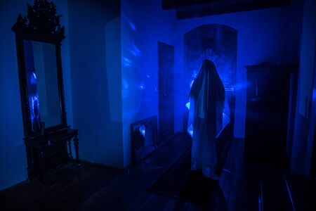 Horror silhouette of ghost inside dark room with mirror. Scary halloween concept. Silhouette of witch inside haunted house with fog and light on background. Selective focusの写真素材