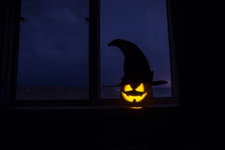 Scary Halloween pumpkin in the mystical house window at night or halloween pumpkin in night on room with blue window. Symbol of halloween in window. Selective focusの写真素材