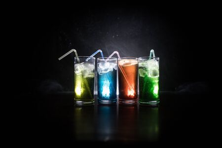 Multicolored glasses filled with alcoholic drinks, with splases of ice cubes falling inside,...