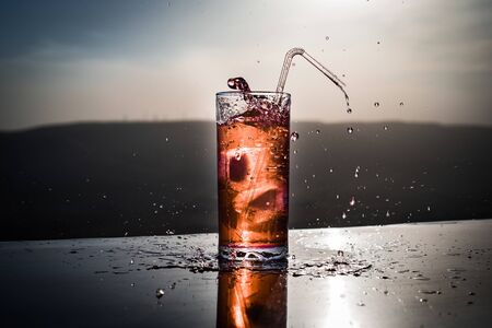 Cooling summer drink concept. Cocktail glasses splashing on sunset. Close up wet glass of cold drink on the terrace. Selective focusの写真素材