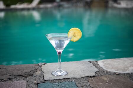 Glass of martini cocktail at swimming pool with forest trees on background. Selective focus. Season and holidays concept.の写真素材