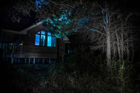 Old house with a Ghost in the forest at night. Horror silhouette at the window. Old building in forest. Surreal lights. Horror Halloween conceptの写真素材