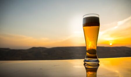 Glass of beer on a beach at sunset. Cooling summer drink concept. Close Up of A Glass of Draught Beer with the Bokeh of Sunlight Background, Soft Focusの写真素材