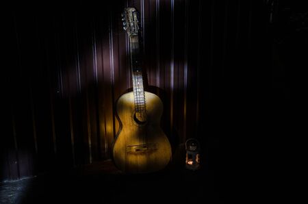 An wooden acoustic guitar is against a grunge textured wall. The room is dark with a spotlight for your copyspace. old broken guitarの写真素材