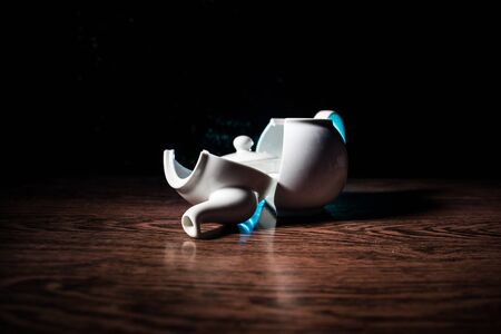 broken teapot on a dark toned foggy background. Pieces of ceramic teapot on wooden table. Selective...