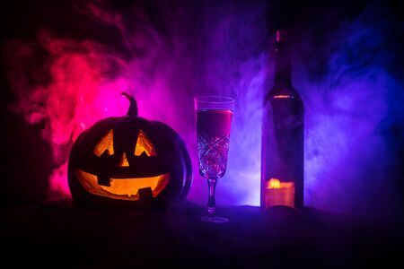 Halloween wine party theme. Glass of wine and bottle with Halloween - old jack-o-lantern on dark toned foggy background. Scary Halloween pumpkinの写真素材