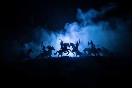 Medieval battle scene with cavalry and infantry. Silhouettes of figures as separate objects, fight between warriors on dark toned foggy background with medieval castle. Selective focusの写真素材