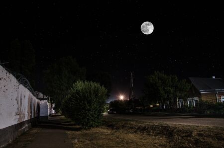 Full moon over quite village at night. Beautiful night landscape of old town street with lightsの写真素材