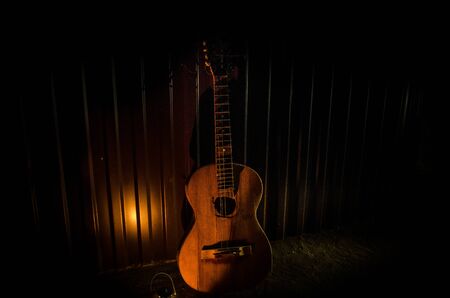 An wooden acoustic guitar is against a grunge textured wall. The room is dark with a spotlight for your copyspace. old broken guitarの写真素材