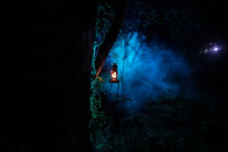 Horror Halloween concept. Burning old oil lamp in forest at night. Night scenery of a nightmare scene. Selective focus.の写真素材