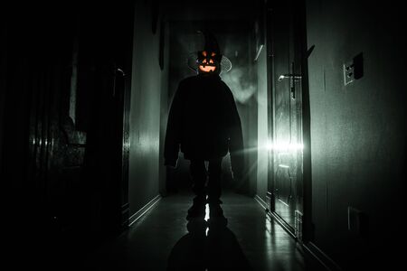Halloween concept. Creepy silhouette in the dark corridor with pumpkin head. Toned light with fog on background.の写真素材