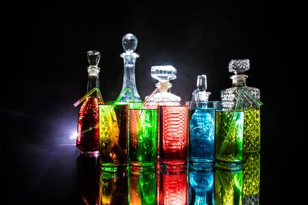 Multicolored glasses filled with alcoholic drinks, with splases of ice cubes falling inside, standing on the mirror surface. Black background. Conceptual, celebrated, commercial design. Closeup.の写真素材