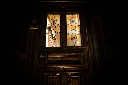 Silhouette of an unknown shadow figure on a old wooden door through a closed glass door. The silhouette of a human in front of a window at night. Scary scene halloween conceptの写真素材