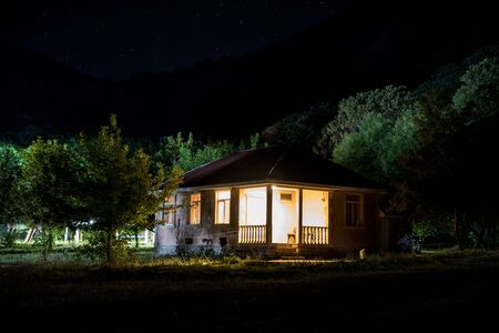 Mountain night landscape of building at forest at night with moon or vintage country house at night with clouds and stars. Summer night. Photo taken with long exposureの写真素材