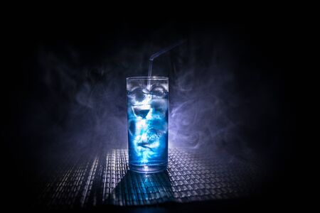 Cocktail glass splashing on dark toned smoky background or colorful cocktail in glass. Party club...
