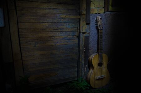 An wooden acoustic guitar is against a grunge textured wall. The room is dark with a spotlight for your copyspace. old broken guitarの写真素材
