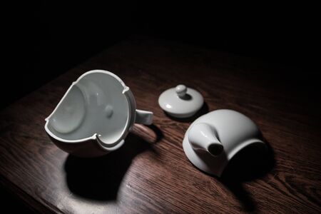 broken teapot on a dark toned foggy background. Pieces of ceramic teapot on wooden table. Selective...