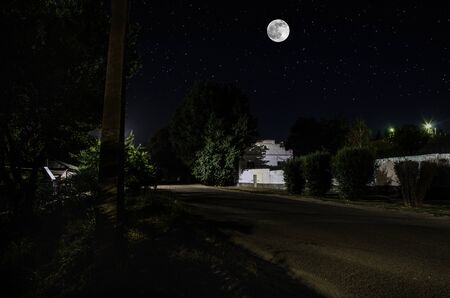 Full moon over quite village at night. Beautiful night landscape of old town street with lightsの写真素材