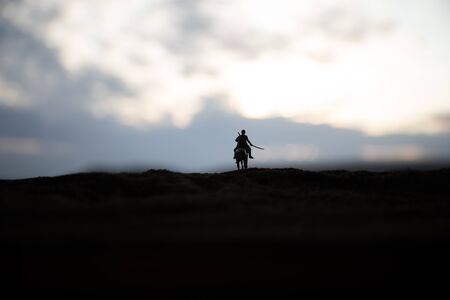 World war officer (or warrior) rider on horse with a sword ready to fight and soldiers on a dark foggy toned background. Battle scene battlefield of fighting soldiers. Selective focusの写真素材