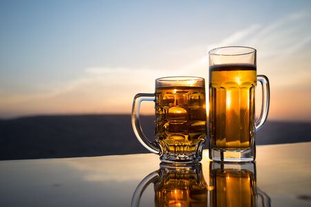 Glass of beer on a beach at sunset. Cooling summer drink concept. Close Up of A Glass of Draught Beer with the Bokeh of Sunlight Background, Soft Focusの写真素材