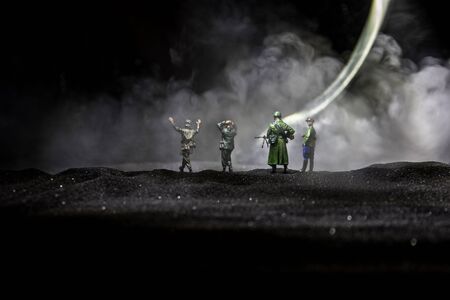 Battle scene. Military silhouettes fighting scene on war fog sky background. A German soldiers raised arms to surrender. Plastic toy soldiers with guns taking prisoner the enemy soldier. Artworkの写真素材
