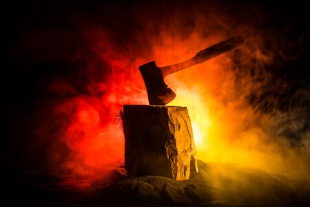 Old ax attached to the tree trunk on horror red foggy background. Scary Halloween theme with maniac...