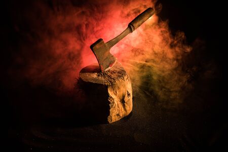 Old ax attached to the tree trunk on horror red foggy background. Scary Halloween theme with maniac...